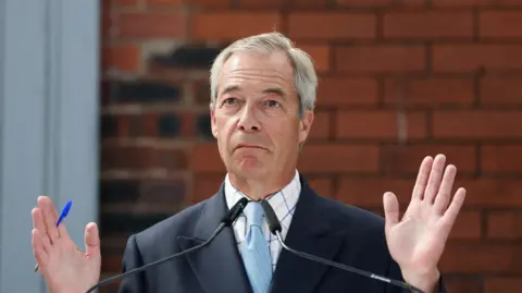 Reuters Reform UK leader Nigel Farage attends a press conference ahead of the Makerfield by-election, in Ashton-in-Makerfield in June. He wears a navy blue blazer, light blue tie and white shirt with blue and beige checks.